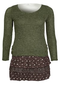 Top lungo a maniche lunghe verde lavorato a maglia con scollatura rotonda, abbinato a una gonna marrone con motivo floreale e volant, impreziosita da pizzo.