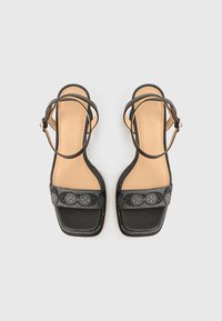 Μαύρα σανδάλια ανοιχτά στα δάχτυλα με υφασμένη λουρίδα που έχει κυκλικά σχέδια, δερμάτινη εσωτερική σόλα και μινιμαλιστικό τετράγωνο σχήμα.