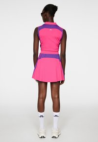 Tät rosa ärmlös klänning med lila detaljer och en plisserad kjol, i kombination med vita strumpor och beige sneakers.