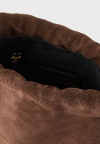 Brązowa zamszowa torba o miękkiej fakturze. Wnętrze wyściełane jest czarną tkaniną i posiada przegródkę zamykaną na zamek dla bezpiecznego przechowywania.