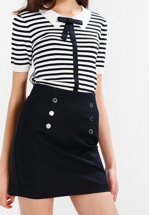 Mustavalkoraidallinen lyhythihainen paita, jossa on valkoinen kaulus ja musta rusetti, yhdistetty mustaan hameeseen, jossa on hopeiset nappikoristeet.