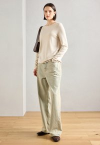 Beige langermet genser, lys grønne baggy jeans, brune spisse sko, minimalistisk design, glatt tekstur, enkle tilbehør, naturlig belysning.