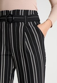 Svartvita randiga byxor har en bred midjeband med en cirkulär svart bältesspänne och sidofickor.