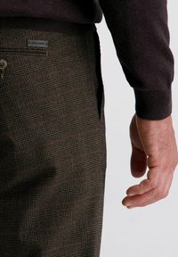 Bruine geruite broeken van textuurstof, met een platte voorkant, zijzakken en een label met "Pierre Cardin" merk. 