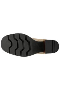Zwarte rubberen zool met een gestructureerd profiel, heeft een beige suède bovenkant, lage hak en een glad houten accent nabij de hak. Maat 37 zichtbaar.