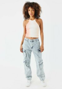 Top corto a coste rosa chiaro con spalline sottili e testo ricamato, abbinato a pantaloni cargo azzurri chiaro con molteplici tasche e zip.