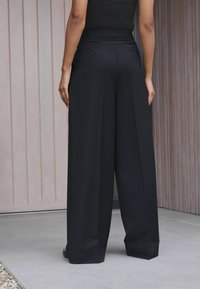 Pantaloni larghi neri con vita alta e silhouette pulita, caratterizzati da un tessuto morbido e un discreto dettaglio della tasca posteriore.