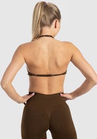 Top halter marrón con un diseño simple y tirante ajustable, combinado con leggings marrones de cintura alta. Textura suave en ambas prendas.