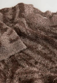 Ruskea, pörröinen tekstiili metallilangalla, jossa on pehmeä rakenne ja kevyt kiilto. Aaltomainen muotoilu eri sävyillä ja syvyydellä.