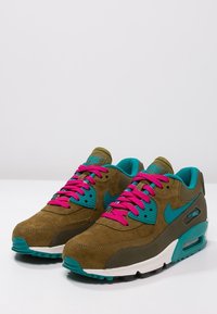 Tenisky Nike Air Max mají svršek z hnědé semišové kůže, tyrkysové akcenty, růžové tkaničky a bílou mezipodešev s viditelnou vzduchovou jednotkou.