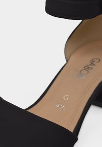 Μαύρο σανδάλι ανοιχτού δακτύλου με τετράγωνο τακούνι, ταμπά εσωτερική σόλα με την επιγραφή "Gabor" και μέγεθος "G 4½", σε λευκό φόντο.