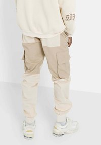Beige cargobyxor med smal passform, som har flera fickor och paneler av kontrasterande beige och krämfärgad tyg. Bärs med vita sneakers.