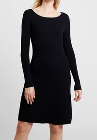 Czarna, prążkowana sukienka z długim rękawem, z dekoltem w łódkę, dopasowanym korpusem, rozkloszowaną spódnicą i bocznymi rozcięciami, wykonana z miękkiego materiału dzianinowego.