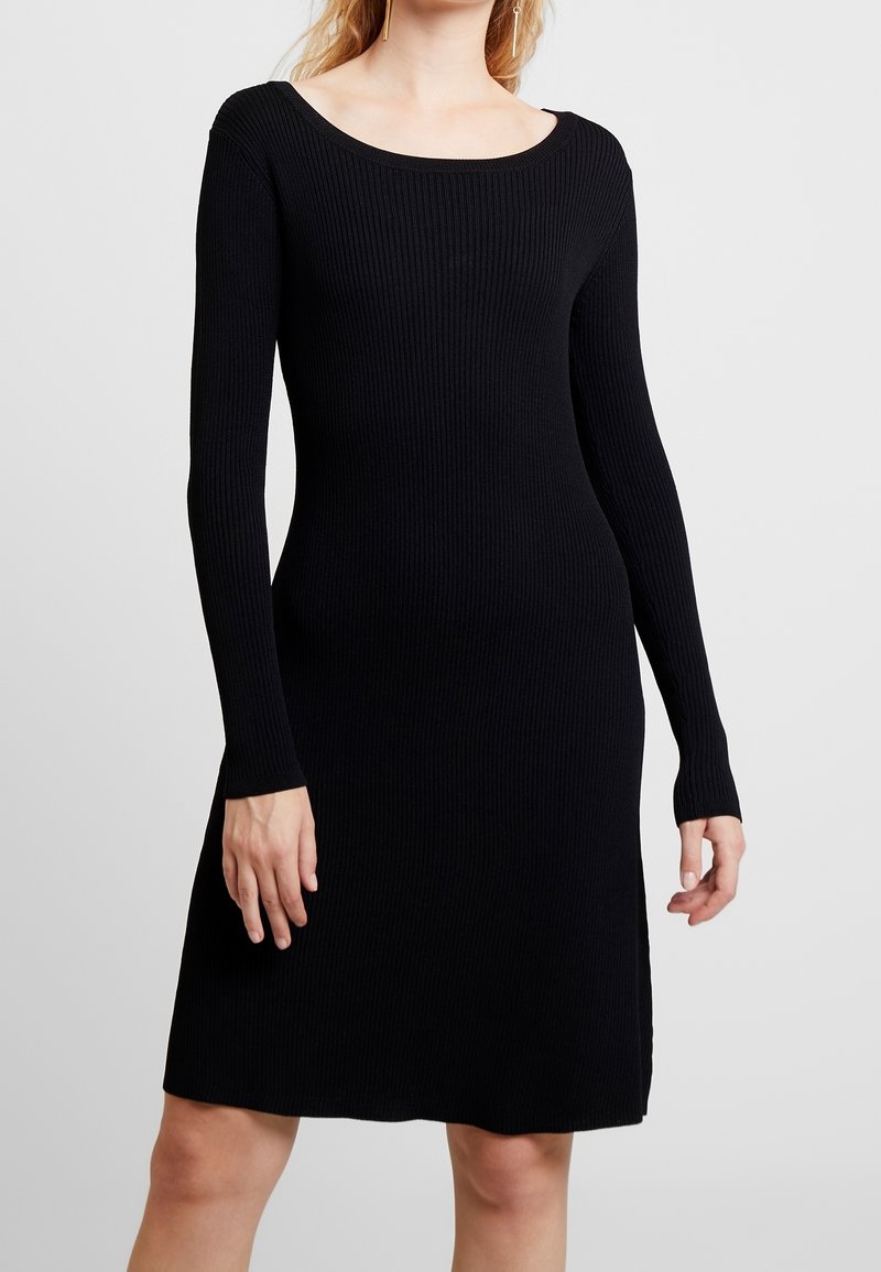 Czarna, prążkowana sukienka z długim rękawem, z dekoltem w łódkę, dopasowanym korpusem, rozkloszowaną spódnicą i bocznymi rozcięciami, wykonana z miękkiego materiału dzianinowego.