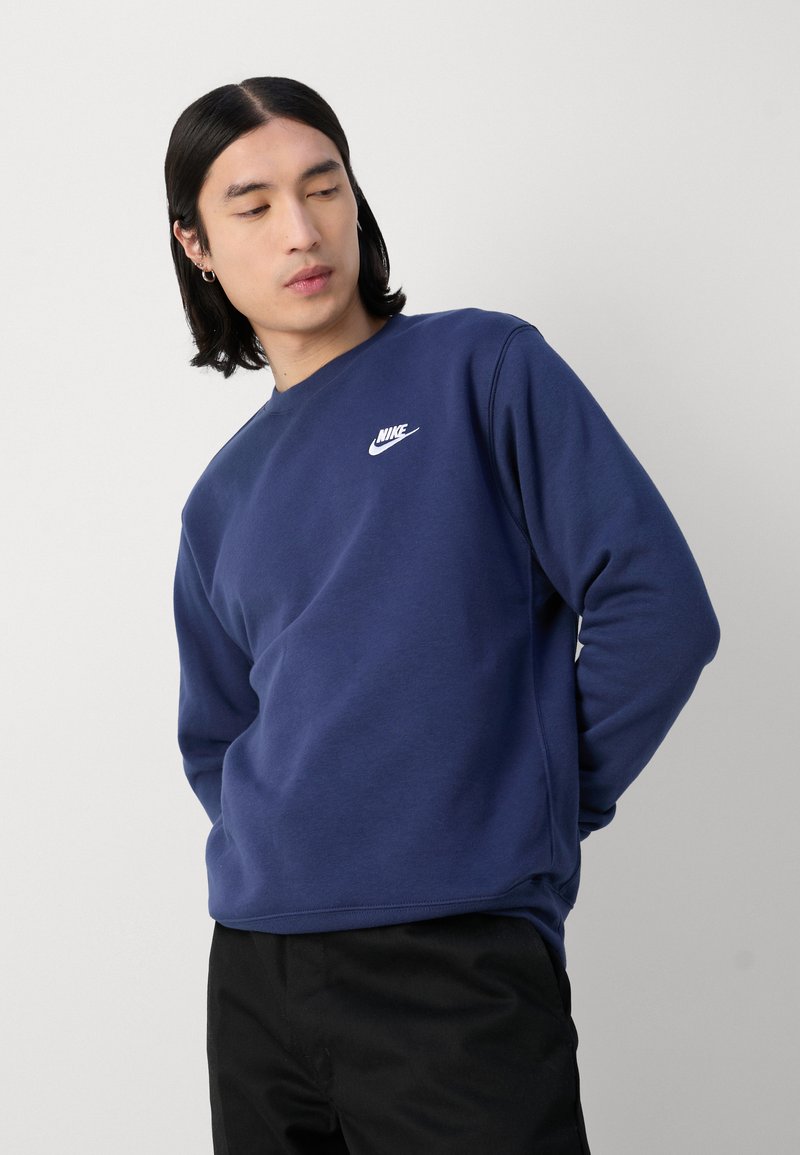 Mörkblå sweatshirt gjord av mjukt material, med rund halsringning, långa ärmar och en vit Nike-logga på vänster bröst.