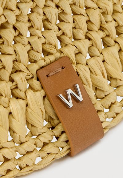 Gros plan sur un matériau en paille tissée avec une sangle en cuir beige ornée d'une lettre "W" en argent attachée.