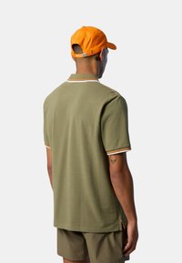 Polo verde oliva con dettagli arancioni e bianchi, maniche corte e spacchi laterali. Abbinato a pantaloni corti coordinati e un cappellino arancione.