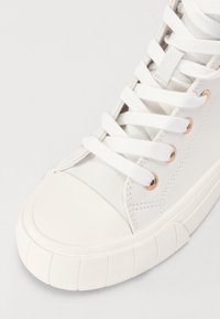 Sneaker bianco in tela con punta rotonda in gomma, lacci piatti e occhielli in oro rosa. Presenta una suola testurizzata e una parte superiore liscia.