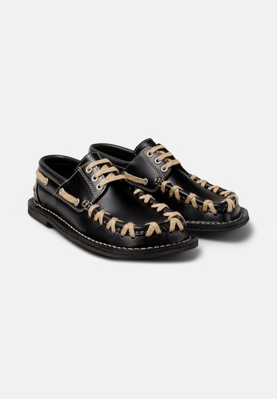 Scarpe in pelle nera con lacci di colore crema a contrasto, dotate di punta arrotondata e dettagli di cucitura lungo la suola e la parte superiore.
