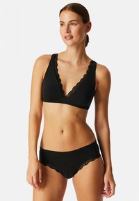 Conjunto de lencería negra que incluye un bralette con borde de encaje y una braguita a juego con un borde ondulado, confeccionado con un material suave y elástico.