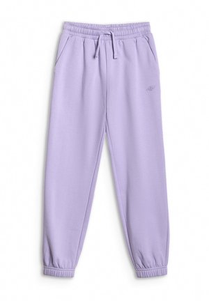 Jong meisje met lang bruin haar, een witte haarband, een crèmekleurige sweater met ritssluiting, lavendelkleurige joggingbroek en witte sportschoenen, staand met handen in de zakken.