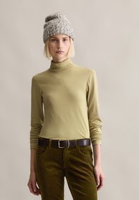 Jasnozielony sweter z długim rękawem i kołnierzem typu turban w zestawie z brązowymi spodniami z kordurowej tkaniny oraz jasnoszarym dzianinowym kapeluszem; całość o gładkiej fakturze.