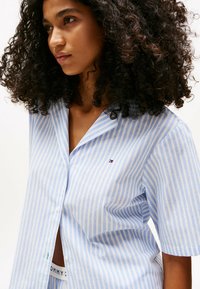 Light blue and white striped short-sleeve button-up shirt with a collar, featuring a small logo and a relaxed fit.