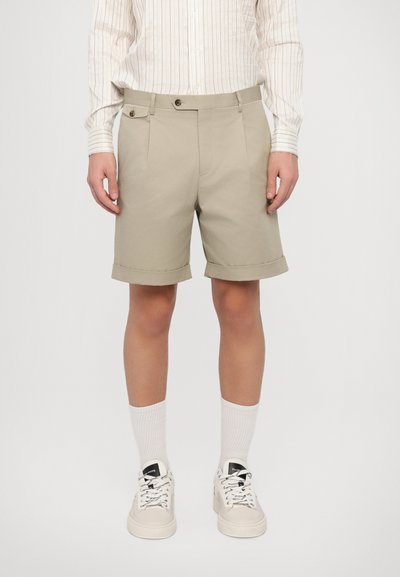 Shorts beiges avec ourlets retroussés, dotés de plis à l'avant et de détails en bouton, associés à des chaussettes blanches et des baskets beige clair.