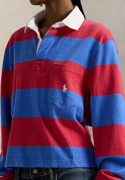 Πολύχρωμο πόλο με μακριά μανίκια σε ρίγες κόκκινου και μπλε, με λευκό γιακά και μικρό κεντημένο λογότυπο στην τσέπη στο στήθος.