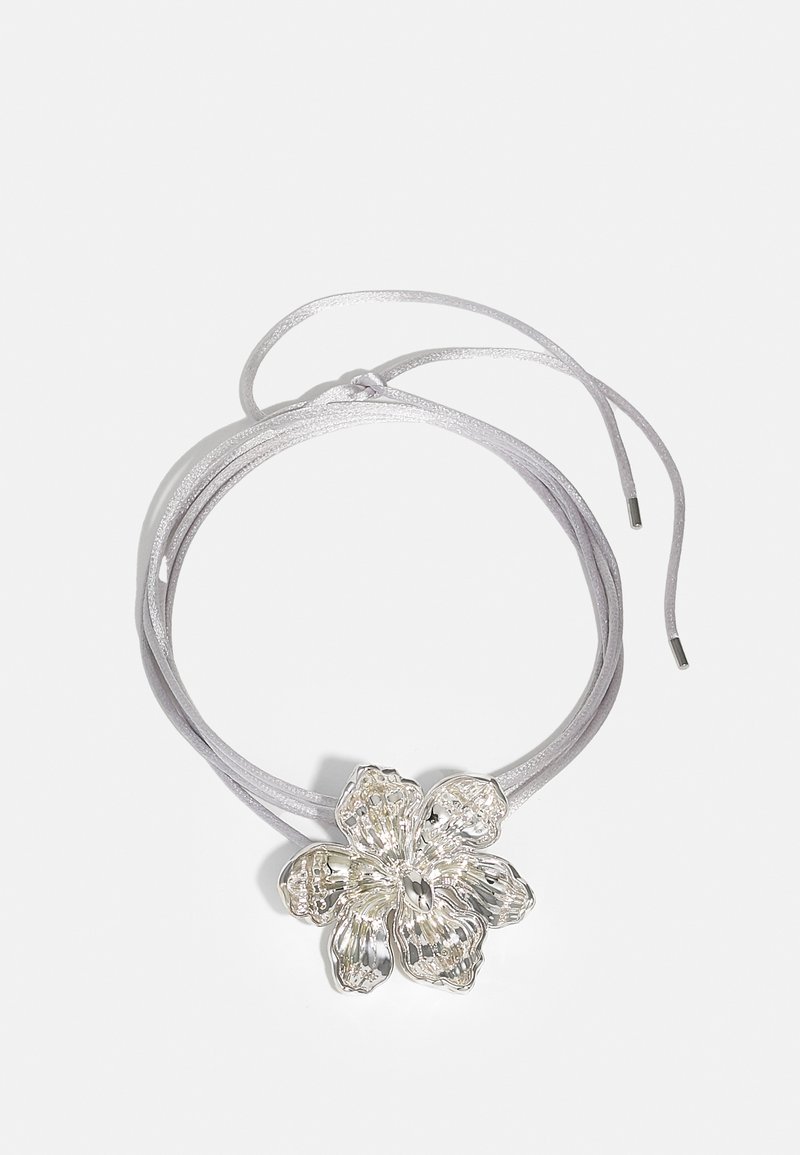 Hõbedane lille ripats hallil paelal. Lillel on tekstuuriga kroonlehed ja keskne detail, paela pikkuse reguleerimiseks.