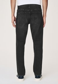 Czarne dżinsy z denimu o prostych nogawkach, z dwoma tylnymi kieszeniami. Czyste wykończenie z subtelną teksturą. Zestawione z granatowymi trampkami.