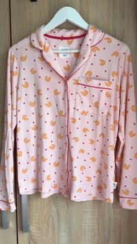 Pink langærmet pyjamastop med krave, med et helhedsmønster af croissanter og røde hjerter, afsluttet med røde kantbånd og en lomme.