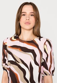 Blusa de mangas curtas com um padrão abstrato multicolorido, apresentando tons de rosa, castanho e laranja. Feita de um tecido leve com um corte relaxado.