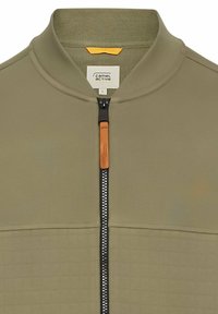 Olijfgroene ritsjack met een textuurpaneel, geribde kraag, zwarte rits en een oranje leren trekkoord. Label maat L aan de binnenkant.