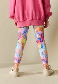Farebné legíny s vírivým mramorovým vzorom v ružovej, modrej a žltej farbe, doplnené o ružovú oversize mikinu a béžové topánky.