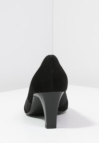 Scarpa nera in suede con tacco alto, punta affusolata, tomaia texturizzata e tacco solido e affusolato. Design semplice ed elegante.