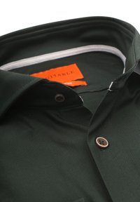Donkergroen shirt met een visgraatstructuur, voorzien van een geknoopte kraag en een bruine knop. Label leest "geschikt."