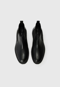 Botas de tobillo de piel negra con un acabado suave, paneles laterales elásticos y una lengüeta en la parte posterior para facilitar su puesta. Suela de goma plana.