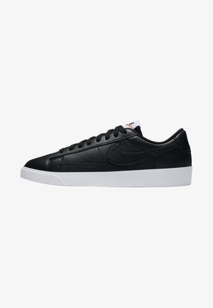 Black leather sneaker with a low profile, white rubber sole, flat laces, minimal branding, and textured finish on the upper.