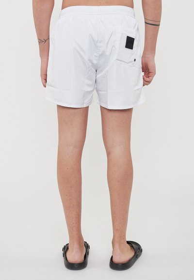 Pantaloni da bagno bianchi realizzati in materiale leggero, dotati di una cintura elastica e di una tasca posteriore con dettagli in etichetta nera.