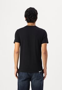 Černé tričko s kulatým výstřihem a krátkými rukávy. Hladká tkanina a běžný střih. Malé logo poblíž lemu. Nosit s modrými džínami.