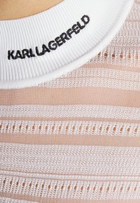 Haut rayé en maille blanche avec col blanc côtelé. "KARL LAGERFELD" brodé en noir sur le col. Texture légère et aérée.