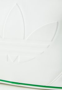 Bela teksturirana torba z embosiranimi logotipom s tremi cvetnimi listi in dvema vodoravnima črtama. Zelen poudarek na dnu. Gladka površina.
