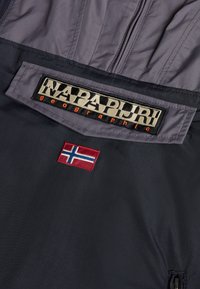 Veste Napapijri avec tissu gris et noir, grand patch logo et drapeau norvégien brodé dans le dos.