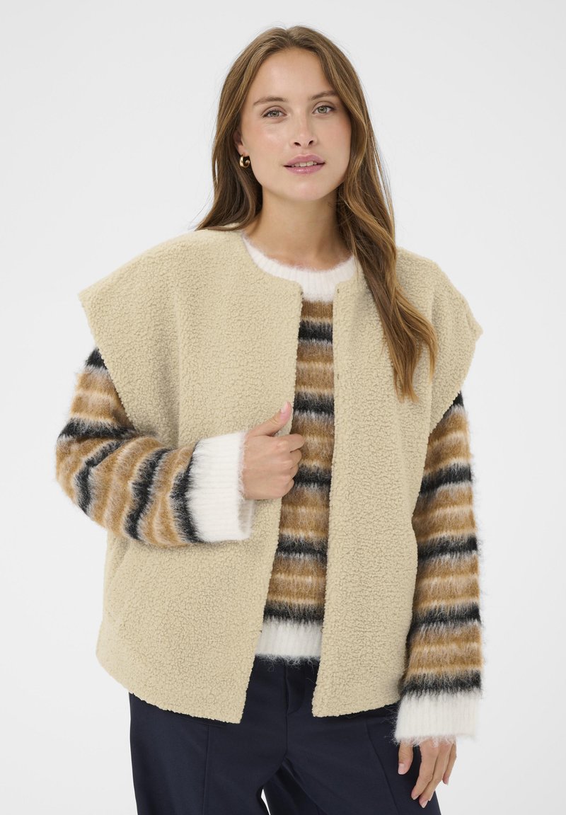 Bežičasti, teksturirani flis kaput s otvorenim prednjim dijelom i širokim ramenima. Uparen s prugastim, višebojnom pletenom puloverom s bijelim detaljima.