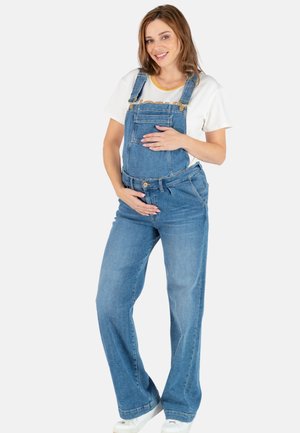 Maternity denim salopette, blauw, met een wijd model, verstelbare schouderbanden, voork pocket, gecombineerd met een wit t-shirt. Geschikt voor comfort en stijl.