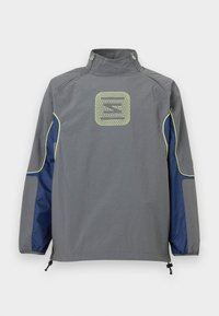 Γκρι μπουφάν με σκούρο μπλε πλαϊνά πάνελ και νέον κίτρινη επένδυση, με γεωμετρικό λογότυπο στο κέντρο του πάνω μέρους της πλάτης και φερμουάρ στο γιακά.