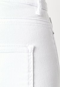 Jeans de mezclilla blanca con un bolsillo trasero con costuras limpias y una textura suave, mostrados parcialmente de lado.