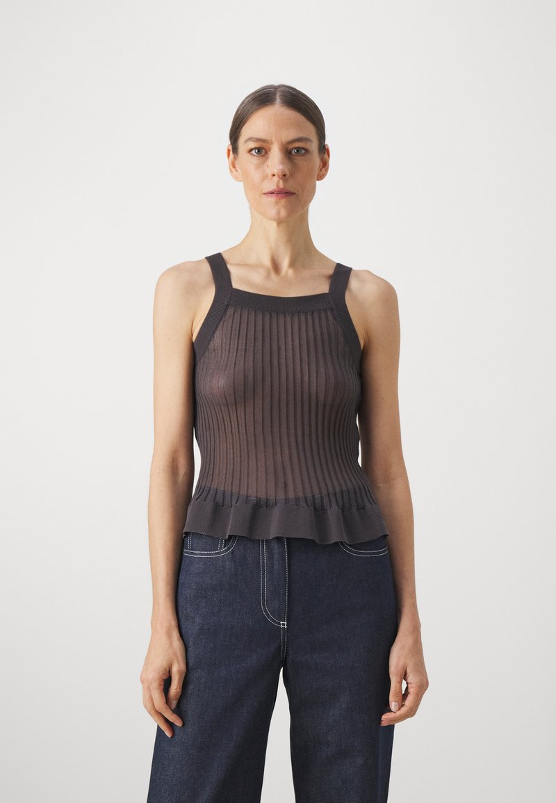 Dark brown sleeveless top made of ribbed fabric, featuring a straight neckline and ruffled hem. Paired with dark blue wide-leg denim pants.