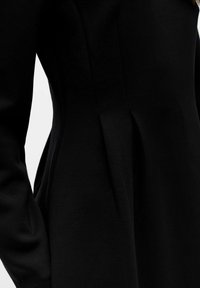 Robe noire présentant une silhouette ajustée avec une texture lisse. Comprend des détails de coutures le long des côtés pour la structure et la forme.